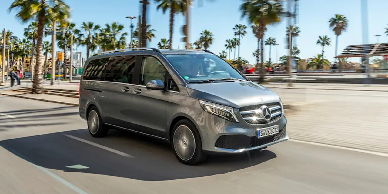 Szary Mercedes minivan jedzie ulicą w słoneczny dzień, otoczony palmami.