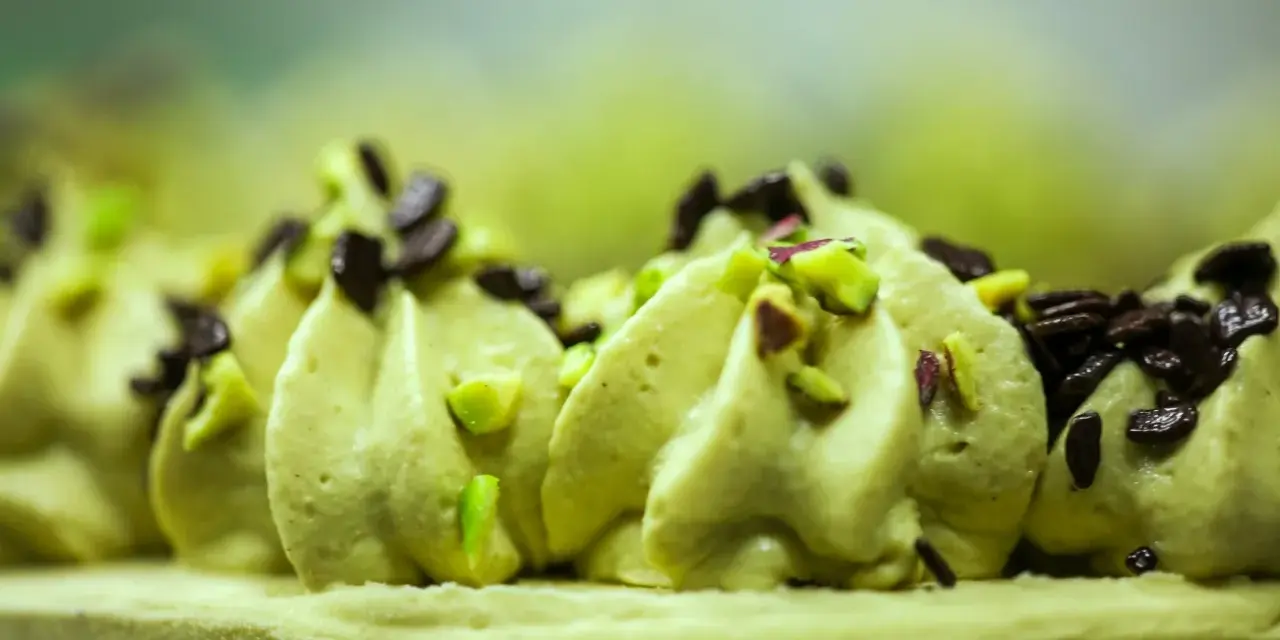 Delikatna masa pistacjowa ozdobiona kawałkami pistacji i czekolady, tworząca apetyczny deser.
