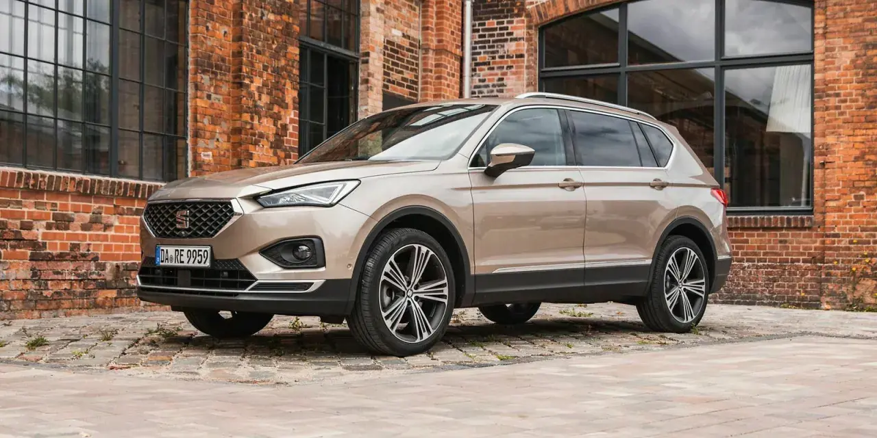 Beiger Seat Tarraco vor Backsteinhaus. Keine Seat Tarraco Probleme hier, nur stilvolles Fahren.