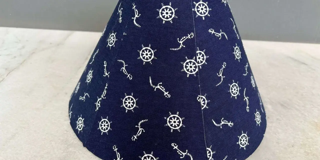 Un abat-jour conique bleu marine orné de motifs d'ancre et de roue de gouvernail. Idéal pour fabriquer un abat-jour en tissu plissé avec une touche marine.