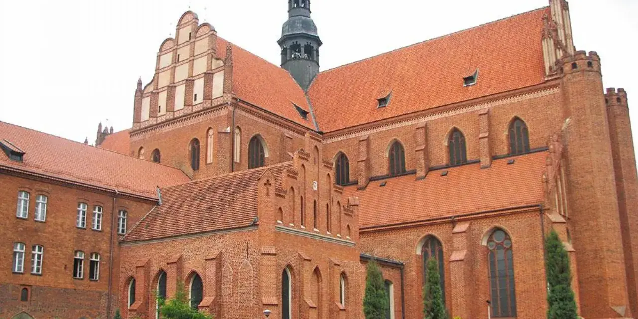 Potężny zamek krzyżacki w Pelplinie, z cegły i czerwonym dachem, góruje nad okolicą.