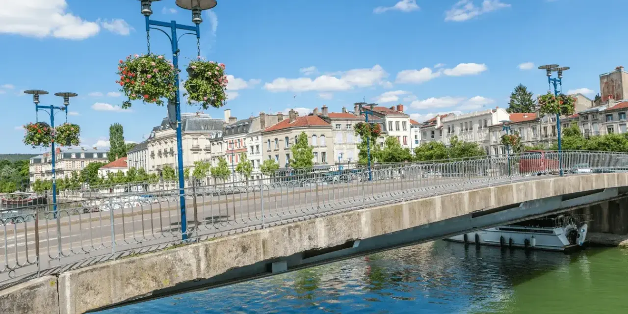 Pont fleuri sur la Meuse, une belle journée pour visiter Verdun en 1 jour. Ville historique avec des bâtiments anciens et un ciel bleu.