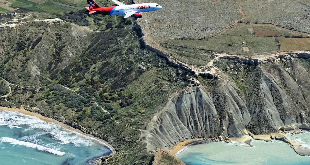 Samolot linii Malta Air przelatuje nad malowniczym wybrzeżem. Widok z lotu ptaka na maltańskie lotniska i krajobraz.