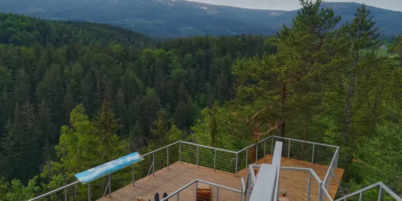 Drewniany punkt widokowy w Karpaczu z widokiem na góry i las. Dwie osoby odpoczywają na tarasie.