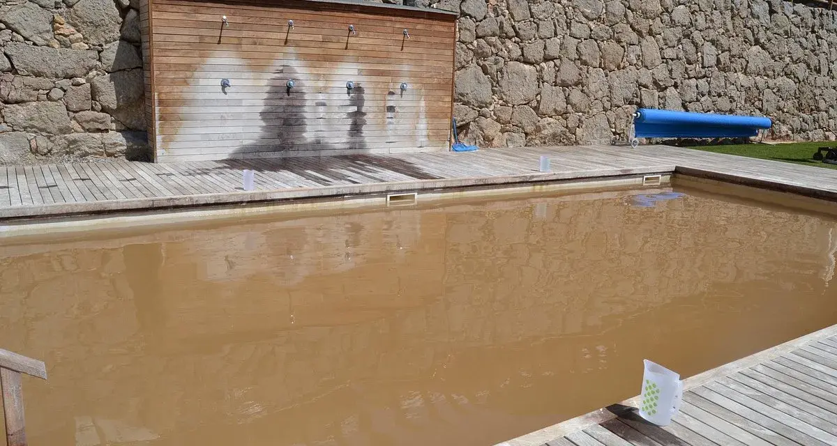Piscina de sal con agua turbia y rodeada de madera. Al fondo, una pared de piedra y duchas.