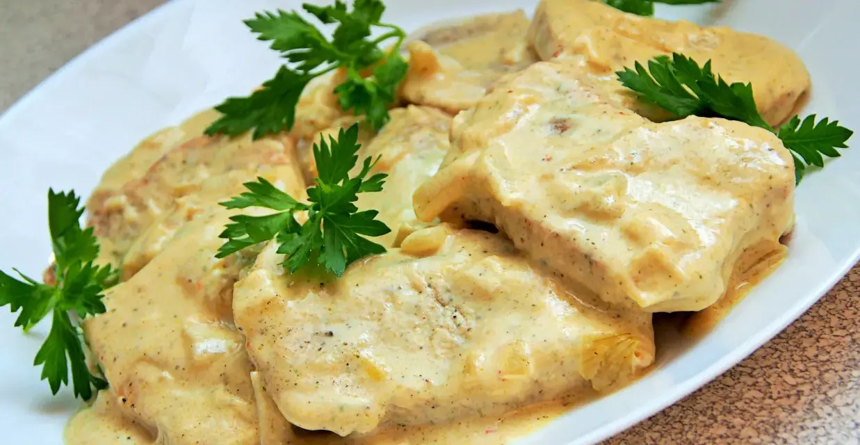 Filet z indyka w sosie śmietanowym, udekorowany natką pietruszki, prezentuje się apetycznie na białym talerzu.