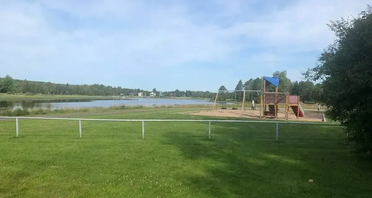 Lekplats med gungor och klätterställning vid en sjö, perfekt för familjer på Malung camping.