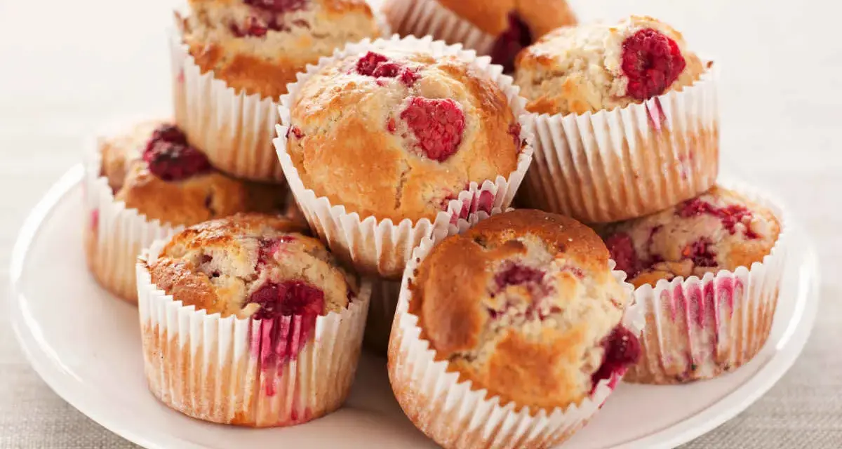 Stos muffinek z malinami na białym talerzu.