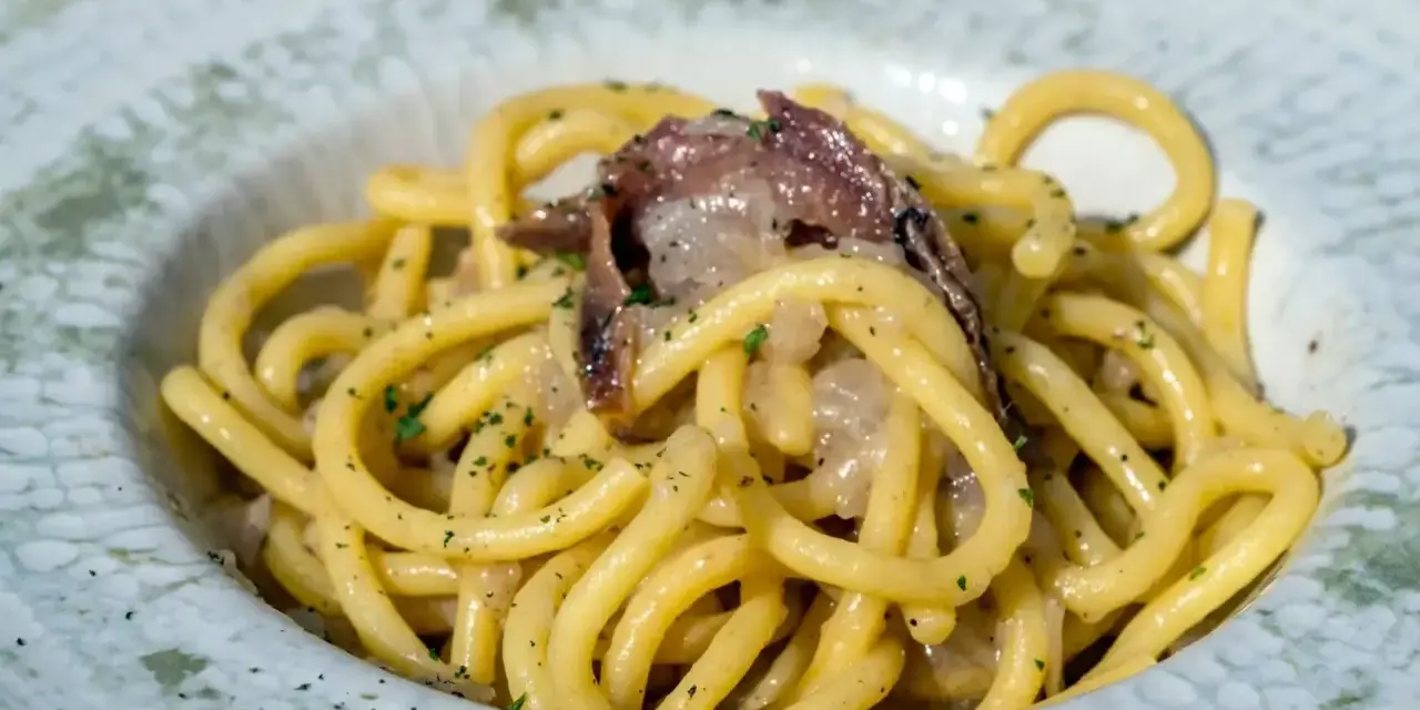 Bucatini con acciughe e cipolla, un classico tra i piatti tipici di Padova, conditi con prezzemolo fresco.