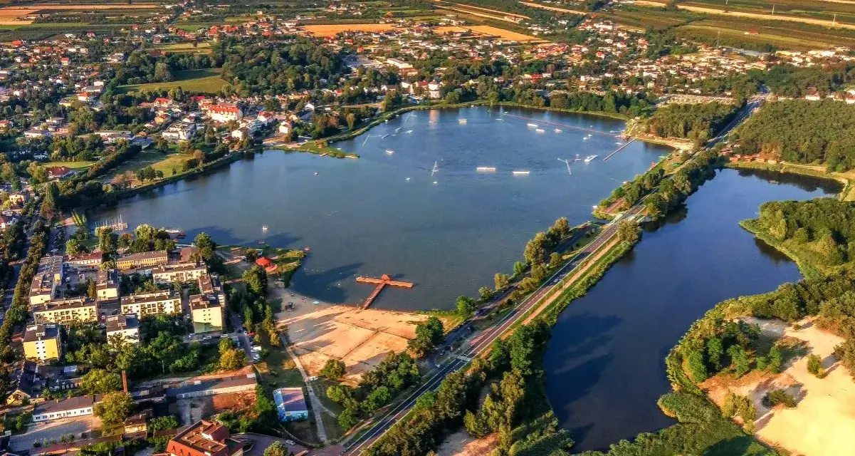 Widok z lotu ptaka na zalew Mrożyczka, z wakeboardzistami, plażą i otaczającą zielenią.