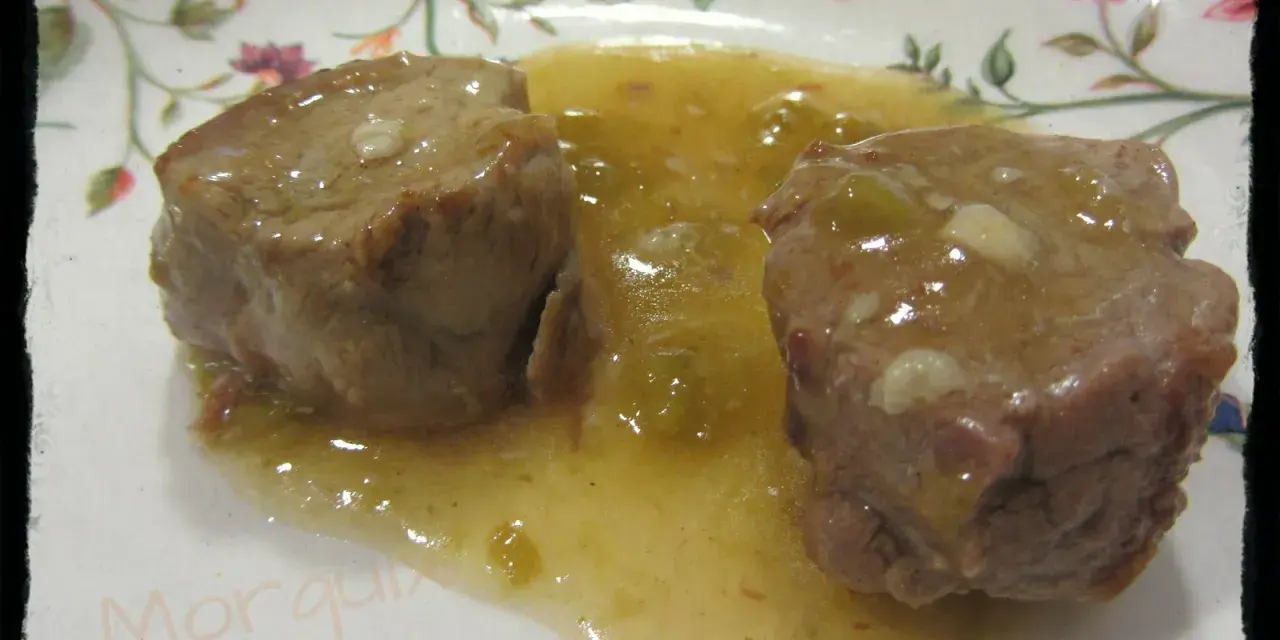 Dos trozos de solomillo al whisky en una salsa dorada, servidos en un plato con flores.