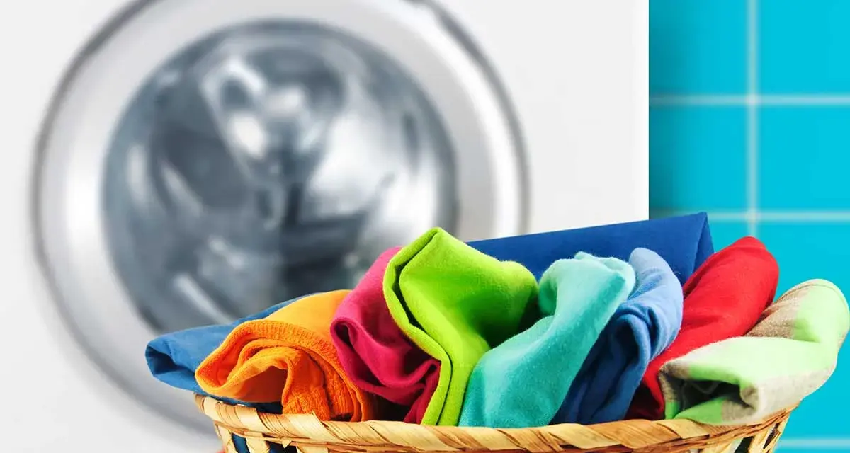 A basket of colorful clothes in front of a washing machine.