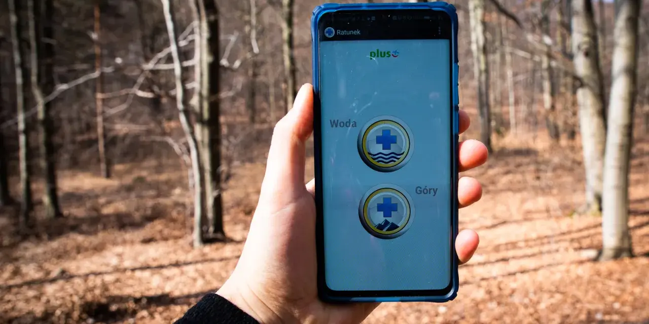 Telefon z aplikacją "Ratunek" do wezwania pomocy w górach lub nad wodą. W tle las.