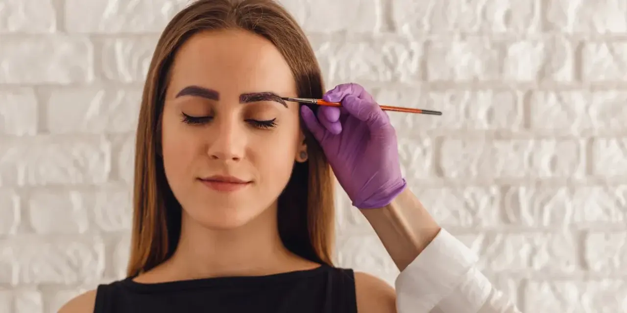 Korekta zbyt ciemnej henny na brwiach. Stylistka nakłada produkt rozjaśniający.
