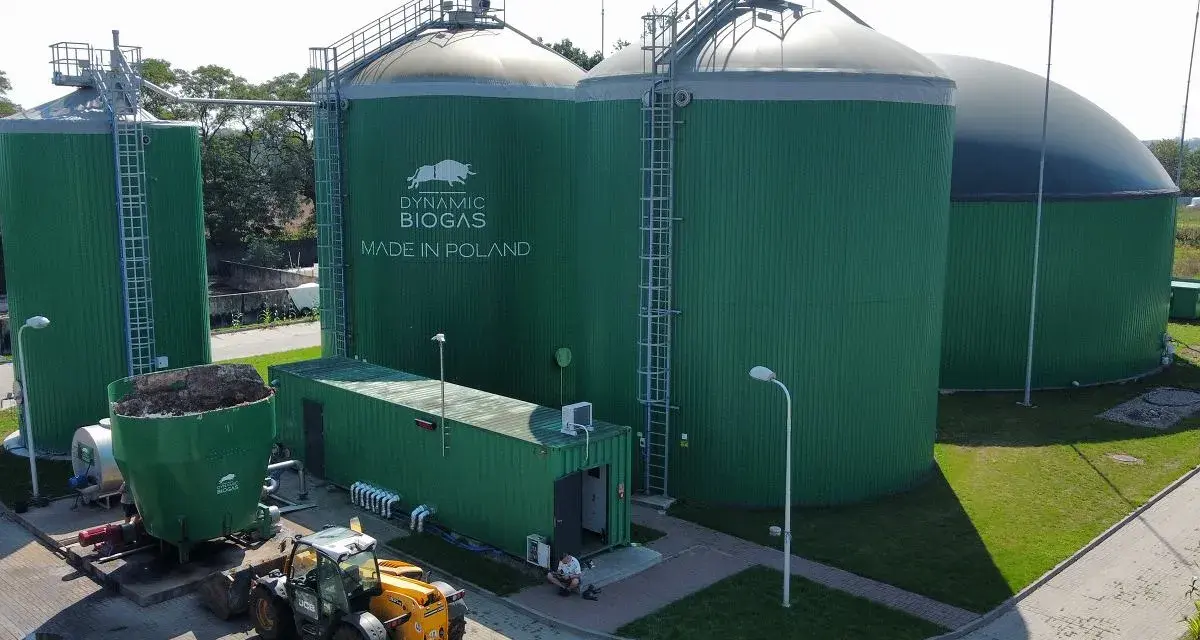 Zielone zbiorniki instalacji biogazowej, z logo "DYNAMIC BIOGAS MADE IN POLAND". Obok ładowarka i kontener.