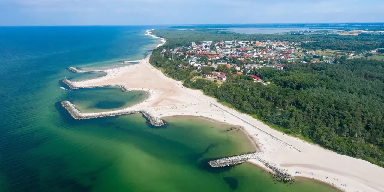 Malownicze plaże w Polsce z kamiennymi falochronami, zielonymi wodami Bałtyku i nadmorskim miasteczkiem w tle.