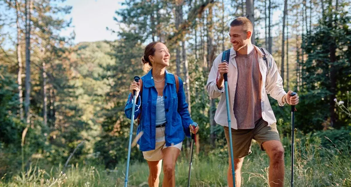 Coppia sorridente fa nordic walking tra gli alberi, godendosi i benefici di questa attività all'aria aperta.