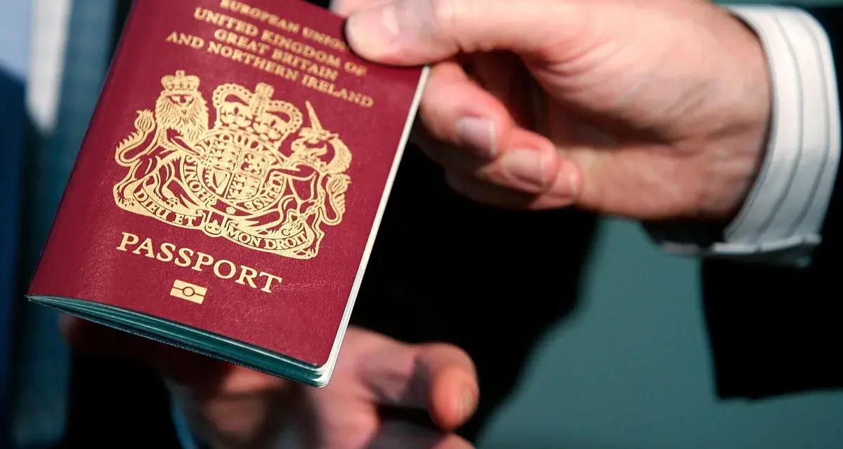Dłoń podaje paszport biometryczny Wielkiej Brytanii. Widoczny herb i napis "PASSPORT".