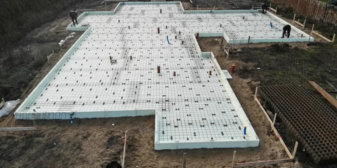 Budowa domu: przygotowane słupy fundamentowe, zbrojenie i izolacja płyty fundamentowej.