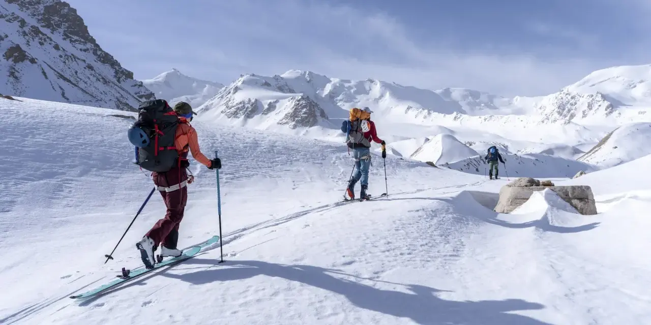 Trois skieurs s'aventurent dans un paysage montagneux enneigé. Une photo ski montagne qui capture l'immensité et la beauté de la nature.