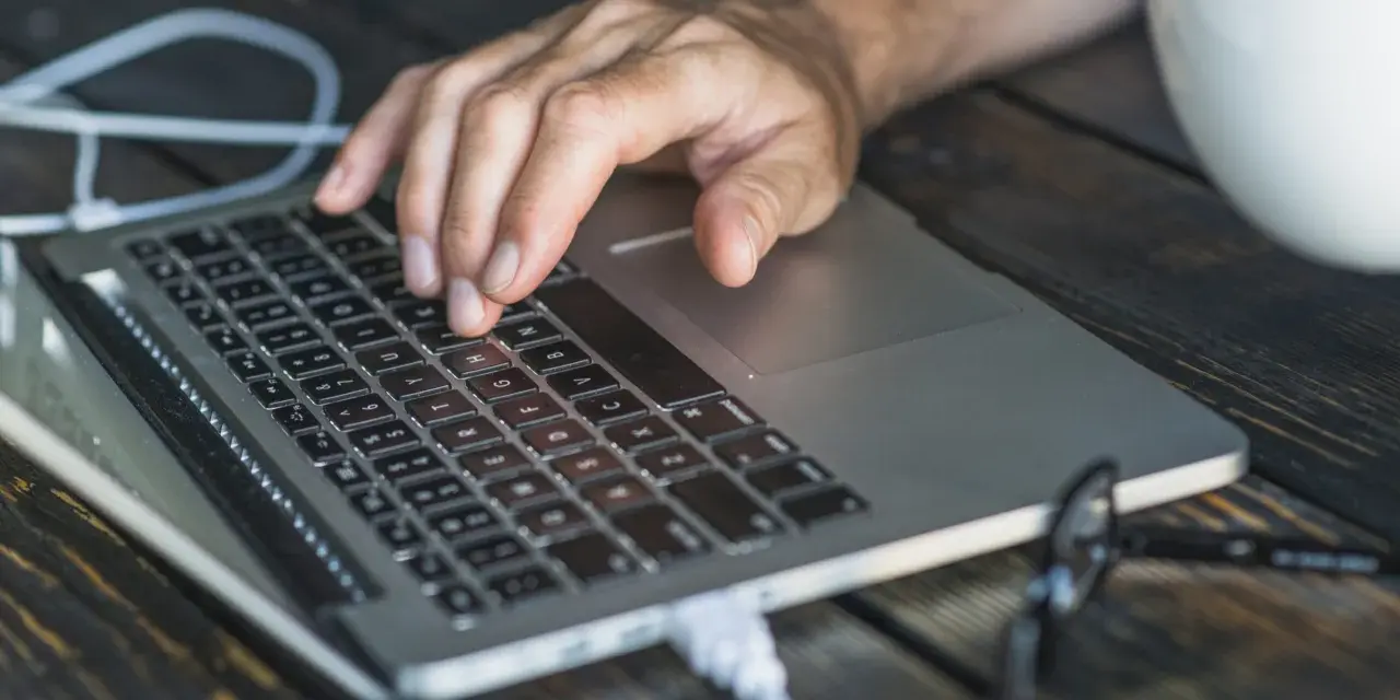 Dłoń na klawiaturze laptopa, przygotowująca się do twardego resetu. Obok biały kubek.