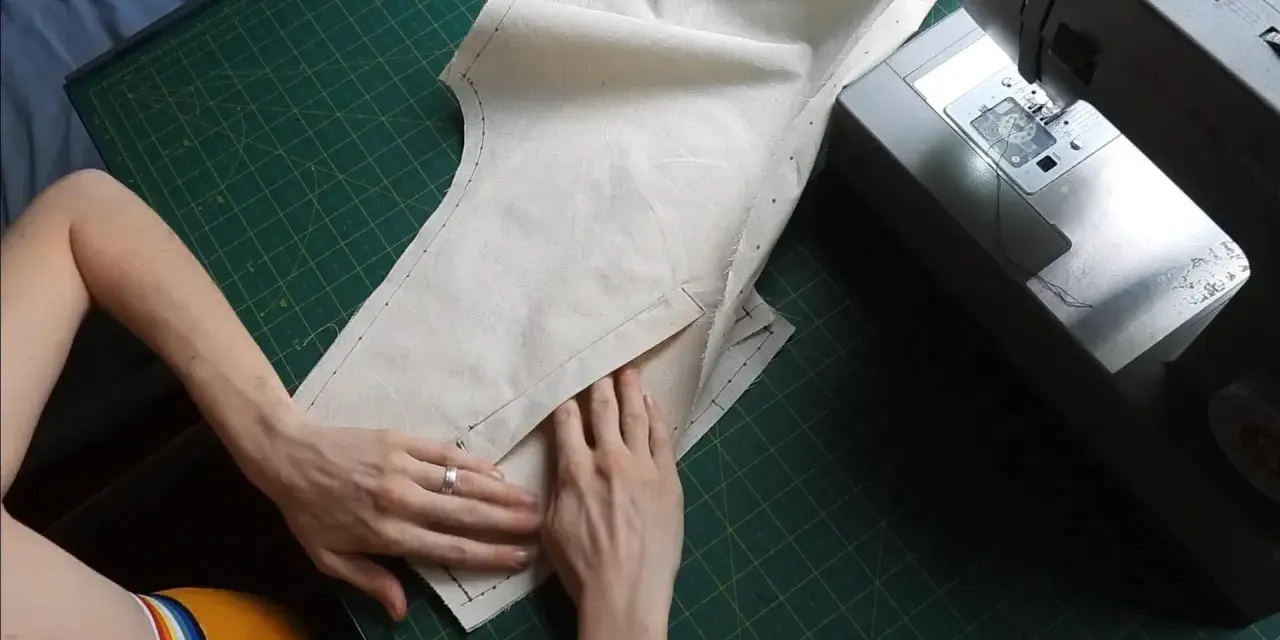 Mains travaillant sur un patron de couture, ajustant un tissu pour une poche raglan, à côté d'une machine à coudre Singer.