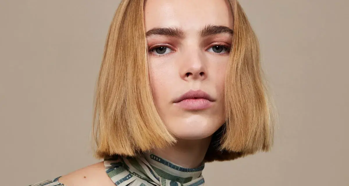 Modelka z subtelnym makijażem i fryzurą bob krótki tył, prezentuje się elegancko w bluzce z wzorem.
