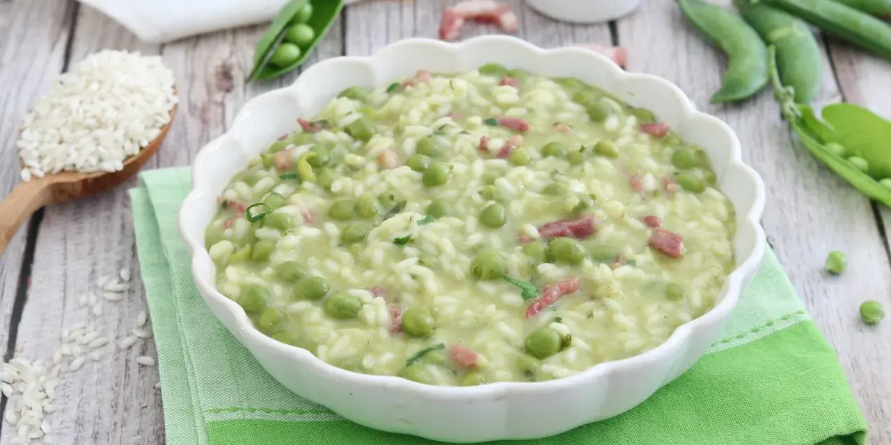 Un cremoso piatto di risi e bisi, con piselli freschi e cubetti di pancetta, servito in una ciotola bianca su un tovagliolo verde.
