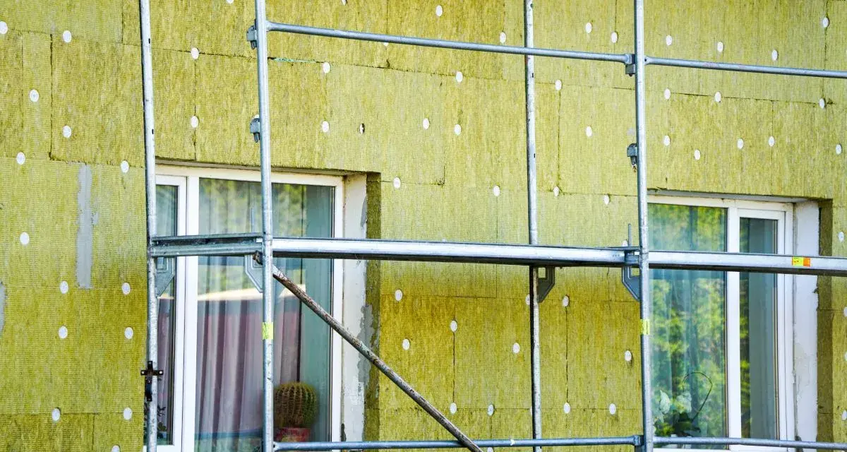 Installazione di un cappotto termico su un edificio, con ponteggi metallici che circondano la facciata isolata. La durata del cappotto termico è garantita da materiali di qualità.