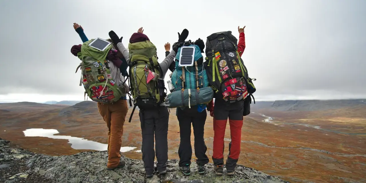 Quatre randonneurs, sacs à dos prêts, contemplent un paysage sauvage. Leur équipement, incluant des panneaux solaires, suggère une préparation pour une liste matériel randonnée 5 jours.