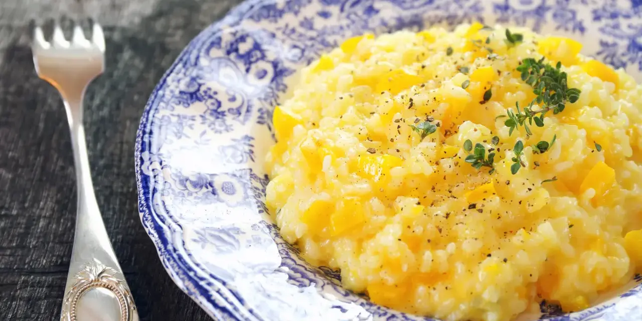 Pyszny, kremowy ryż do risotto z kawałkami dyni, posypany świeżym tymiankiem i pieprzem. Obok leży ozdobny widelec.