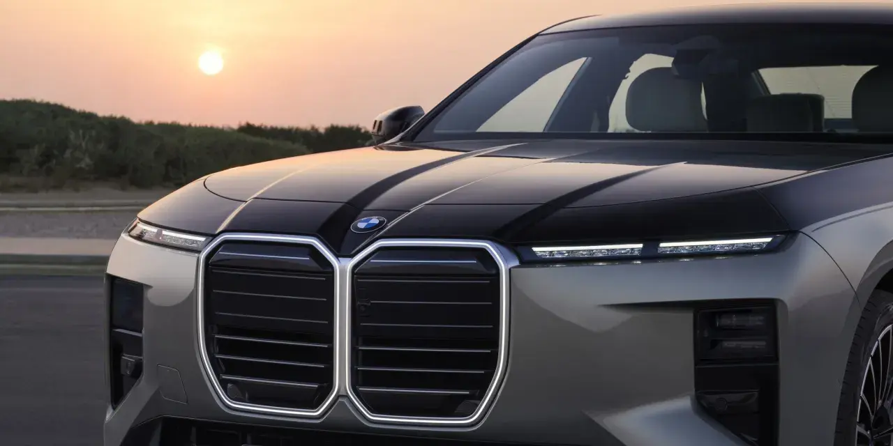 Przód luksusowego BMW M7 z podświetlaną atrapą chłodnicy i nowoczesnymi światłami, na tle zachodzącego słońca.