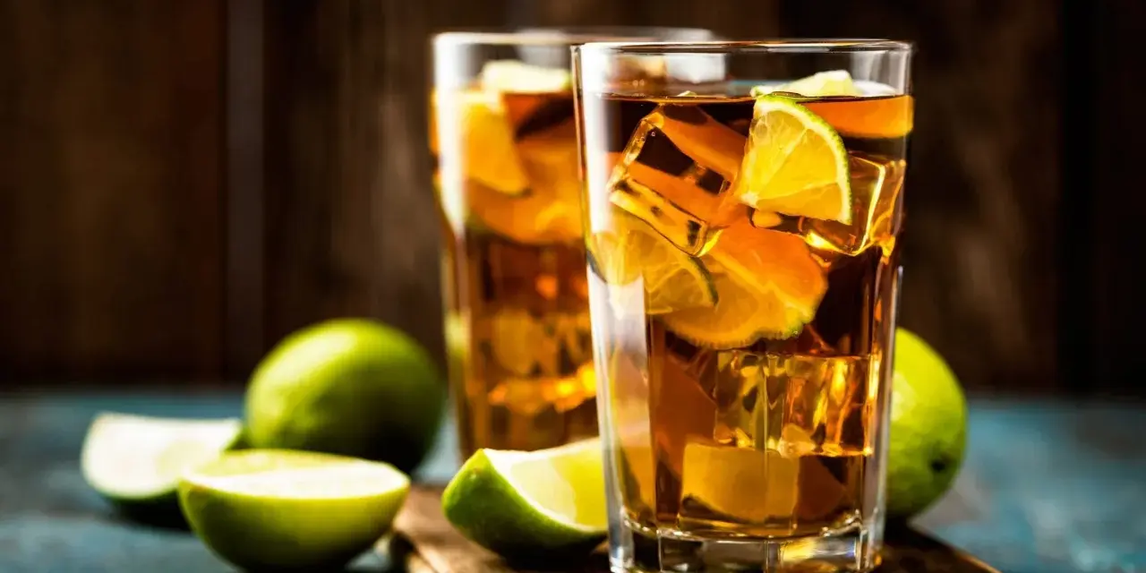 Dwa orzeźwiające drinki: Long Island Iced Tea czy Tokyo Tea, z lodem i limonką, na drewnianej desce.