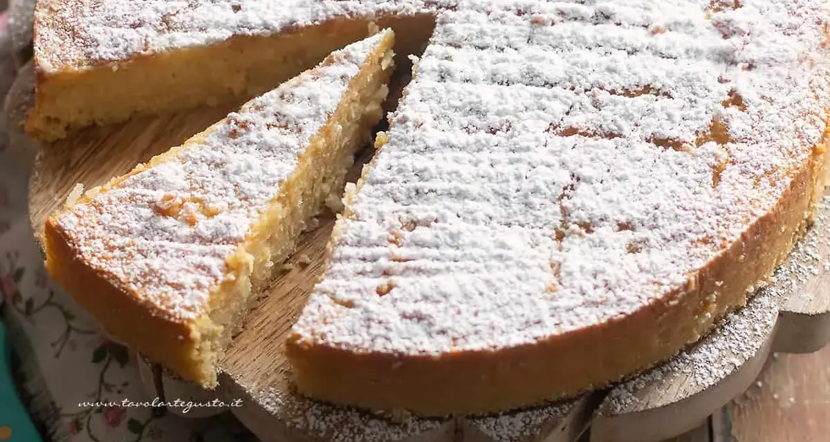 Una deliziosa torta di riso, cosparsa di zucchero a velo, su un tagliere di legno. Una fetta è già stata servita.