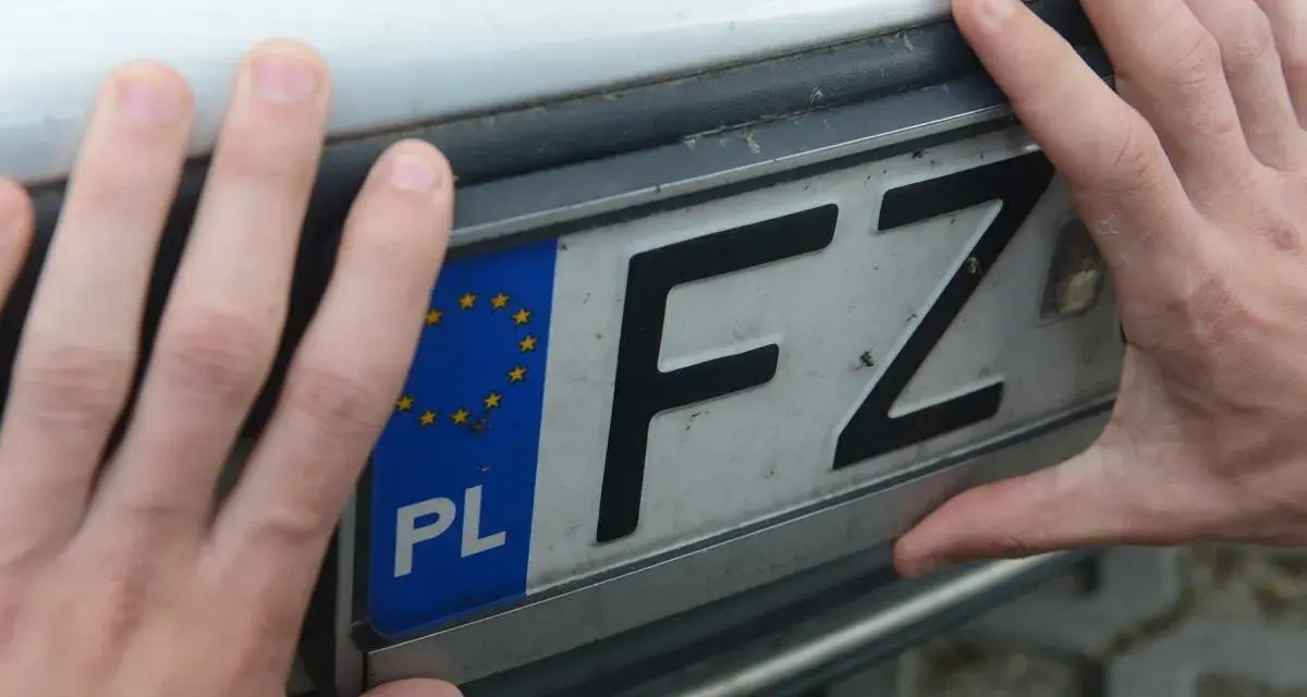 Dłonie trzymają tablicę rejestracyjną z oznaczeniem PL i literami FZ. Może to być związane z czasowe wyrejestrowanie pojazdu.