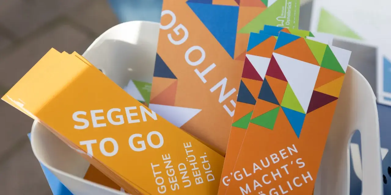 Bunte Karten mit der Aufschrift "Segen to go" und inspirierenden Botschaften wie "Gott segne und behüte dich" liegen in einem Korb.