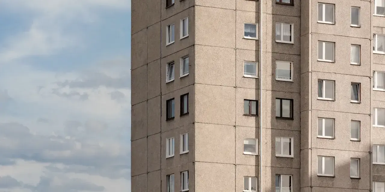 Szare bloki mieszkalne, każde mieszkanie od miasta z oknami wychodzącymi na niebo. W oddali widać komin.