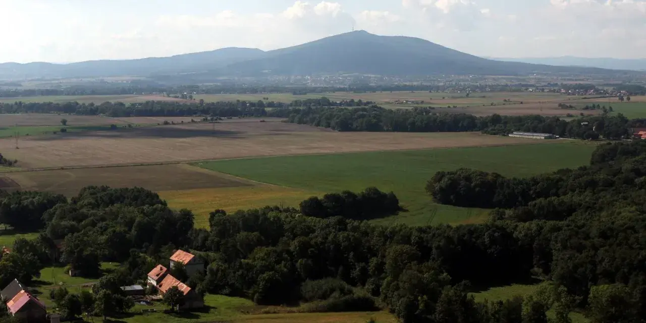 Widok na górzystą okolicę obok Wrocławia z polami, lasami i kilkoma domami.