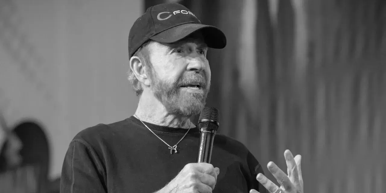 Chuck Norris, mimo swojego wieku, wciąż ma charyzmę. Mówi do mikrofonu w czapce z daszkiem.
