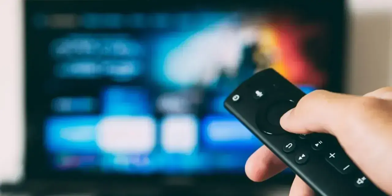 Dłoń trzymająca pilot do telewizora LG, ekran pokazuje menu. Dowiedz się, jak wyłączyć lektora w telewizorze LG.