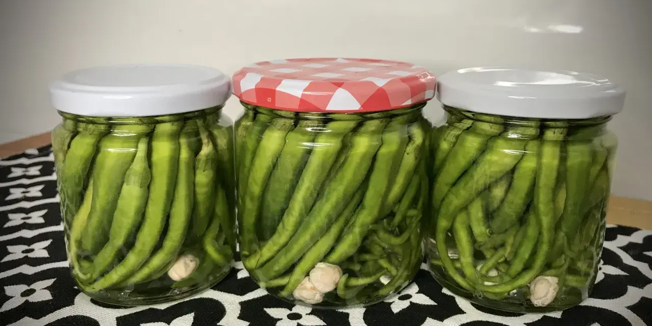 Tres frascos de vidrio llenos de piparras en vinagre, con ajos en el fondo. Uno tiene tapa a cuadros rojos y blancos.
