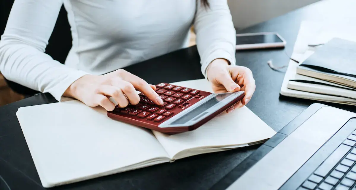 Kobieta liczy wydatki na własne cele mieszkaniowe, przygotowując PIT-39. Na biurku notatnik, kalkulator i laptop.