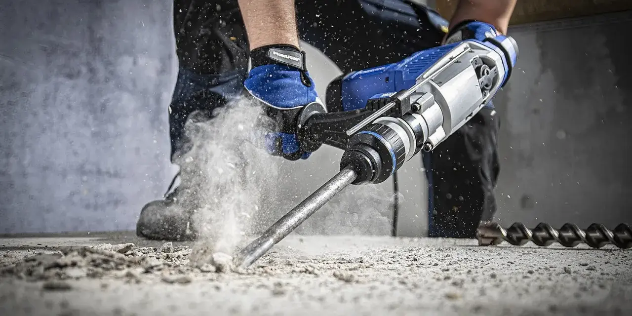 Wiertarka udarowa kruszy beton, generując pył. To narzędzie do ciężkich prac budowlanych.