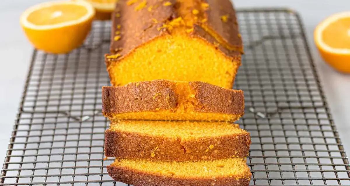Un delicioso bizcocho de naranja, recién horneado y cortado en rebanadas, reposa sobre una rejilla.