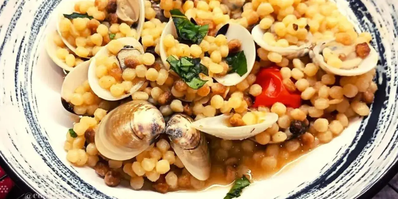 Piatto di fregola con vongole, pomodorini e basilico fresco. Un classico sardo che profuma di mare.