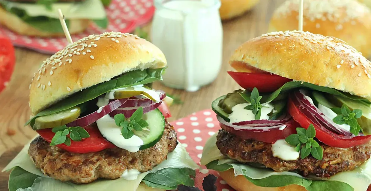 Dwa soczyste burgery wołowe z dodatkami na drewnianym tle.