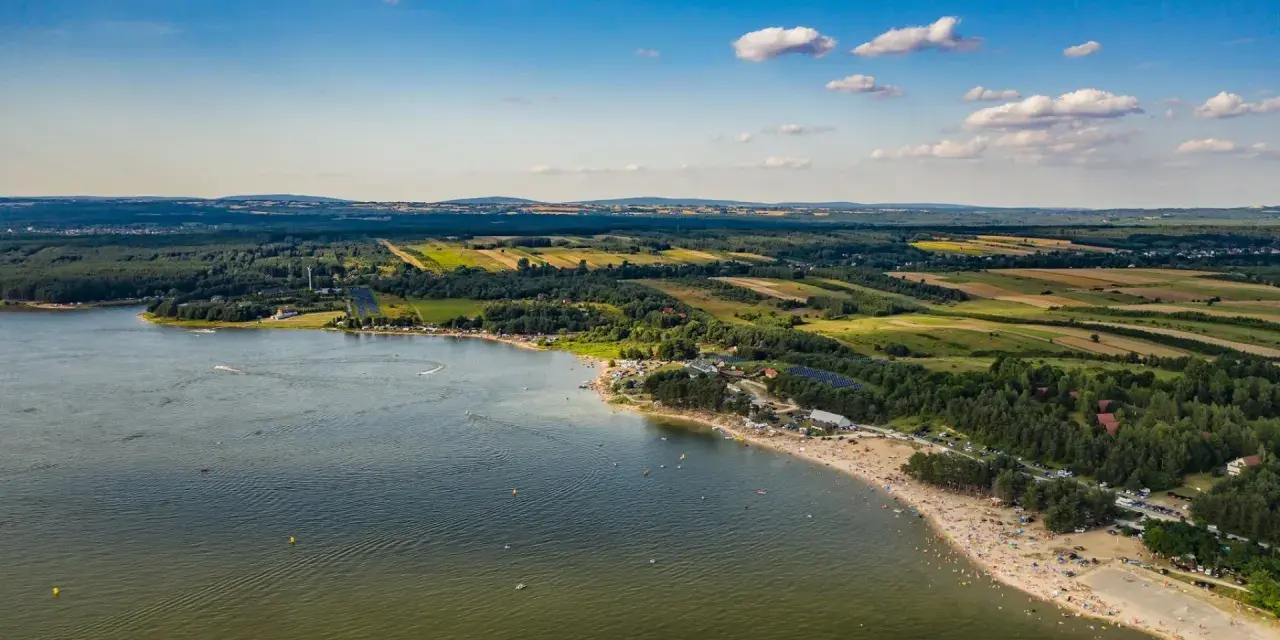 Letnie słońce nad **Jeziorem Chańcza**. Tłumy plażowiczów, zielone lasy i pola tworzą malowniczy krajobraz.