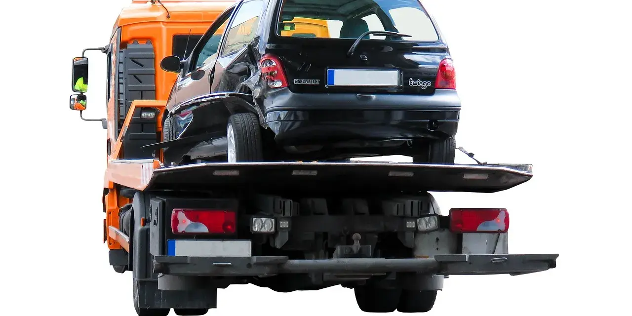 Pomarańczowy holownik zabiera uszkodzonego czarnego Renault Twingo po wypadku na autostradzie.