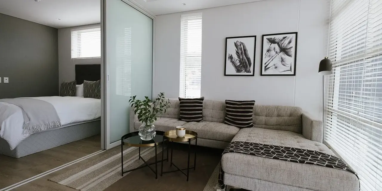 Nowoczesny salon z przesuwnymi drzwiami, za którymi widać sypialnię. Sofa, stoliki, obrazy.