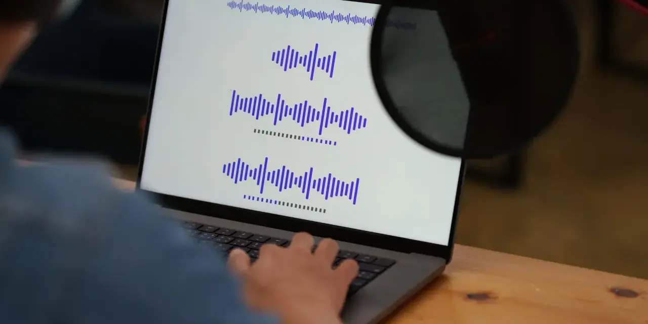 Osoba pracuje przy laptopie, na ekranie widoczne są wykresy fal dźwiękowych, co może być związane z tworzeniem adlibów.